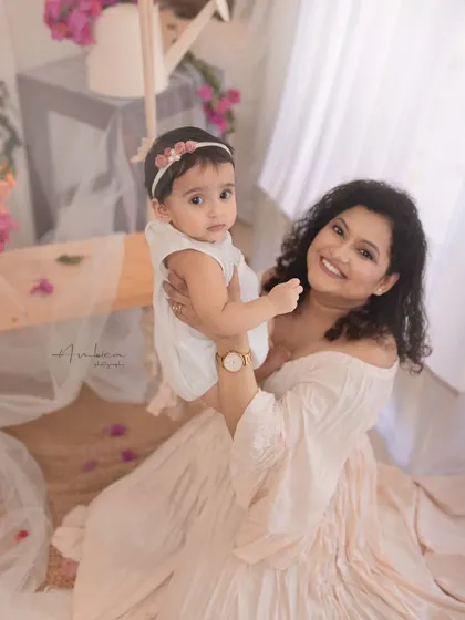 A mother holds her baby girl in a studio filled with bougainvillea. The soft, floral setting and their loving interaction create a warm and beautiful portrait.