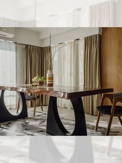 A full view of the live-edge dining table with its unique circular metal bases. The set is paired with custom-made dining chairs that have upholstered seats and curved wooden backrests, creating a modern and organic dining space.