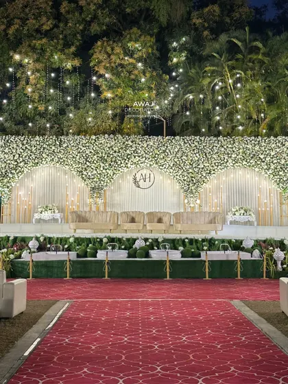 The full view of the white floral stage with a red carpet aisle, contrasting beautifully with the lush green lawn for a classic and grand wedding look.