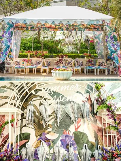 A tropical-themed setup with vibrant floral prints on the canopy and cushions. The backdrop features a playful umbrella installation, adding a touch of summer fun to this outdoor event.