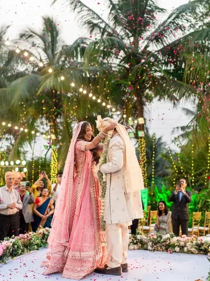A sweet moment during the varmala exchange, with the bride smiling as she places the garland on the groom.