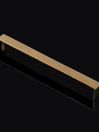 A minimalist shot of a brass-finished rectangular handle on a reflective black surface. This clean, graphic style is ideal for architectural hardware catalogs.