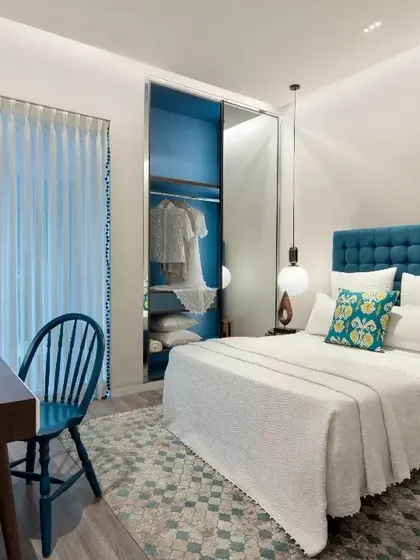 A vibrant bedroom in the Emaar DigiHomes project. The use of bold blue on the wardrobe and headboard, paired with unique pendant lighting, creates a youthful and energetic personal space.