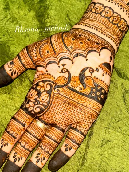 A close-up of the palm, highlighting two graceful peacocks amidst a backdrop of fine lattice work. The design is framed by lotus flowers and intricate borders, showing a mastery of detail.
