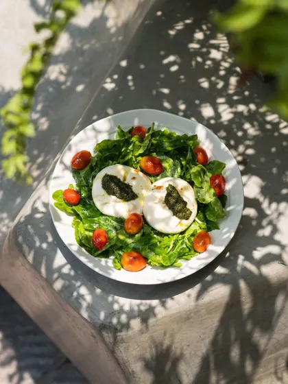 Our burrata served on a bed of fresh greens with cherry tomatoes and a drizzle of pesto. This dish is a celebration of freshness, from the cheese we make ourselves to the vibrant produce.