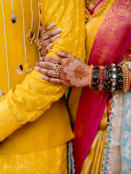 A detail shot focusing on the bride's hands, adorned with mehendi and bangles, holding the groom's arm.