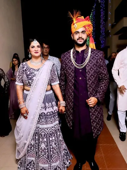 An open jacket Indo-Western in a deep wine color with Lakhnavi fabric. The groom's outfit is designed to complement the intricate work on the bride's grey and purple lehenga.