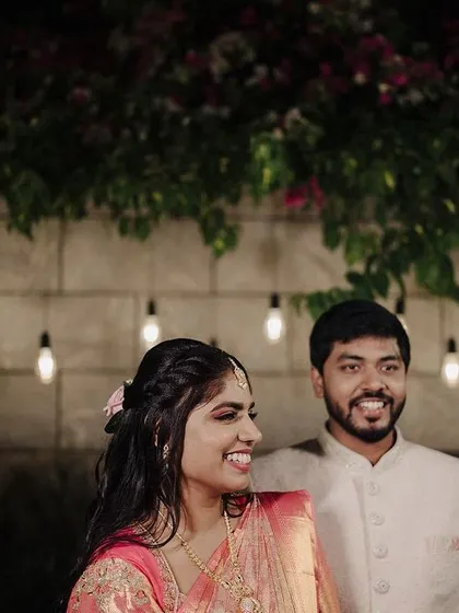 A sweet, candid portrait from an engagement shoot. The couple's smiles and the romantic lighting from the bulbs in the background create a warm and intimate atmosphere.