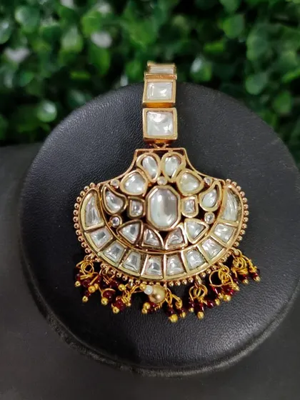 A delicate kundan maang tikka with a square design and red bead drops. This is a simple yet elegant piece for any occasion.
