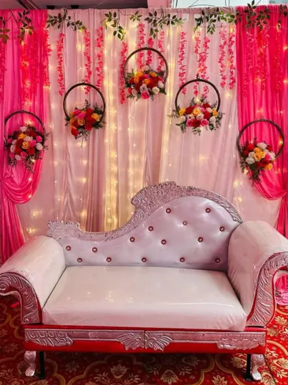 A simple and elegant stage decor with a pink curtain backdrop and hanging floral hoops, perfect for an engagement or naming ceremony.