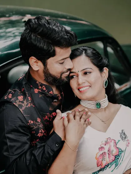 A close and affectionate portrait of a couple leaning against a vintage car, showcasing their traditional attire and the classic vehicle.