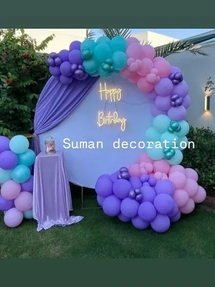 An outdoor garden party setup with a purple, teal, and pink balloon garland on a white circular backdrop.