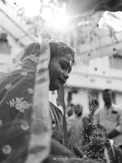 A black and white shot of the bride during the 'Talambralu' rice-showering ceremony. The motion of the rice and her serene expression create a powerful, timeless image.