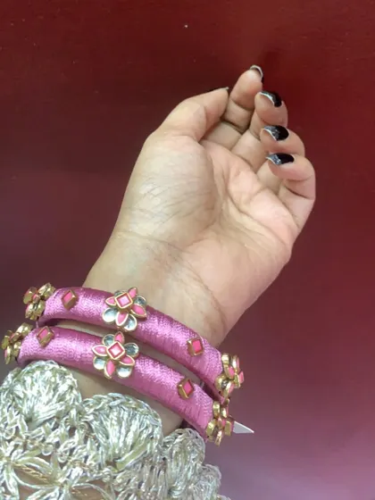 These delicate pink silk thread bangles are adorned with small floral meenakari charms. They are a sweet and simple design, perfect for any occasion.
