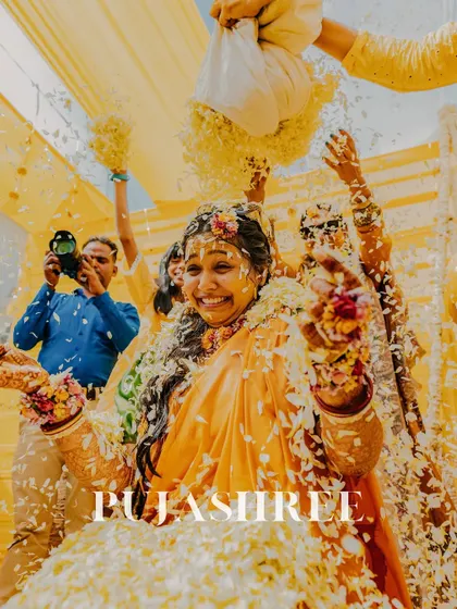 A shower of flowers for the bride. This joyful shot of Pujashree during her Haldi ceremony captures her infectious smile and the celebratory spirit of the moment.