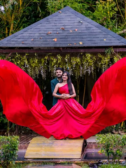 The single-shoulder red gown flows beautifully, creating a dramatic and fashionable statement. This pose at the classic gazebo is perfect for a stylish and modern pre-wedding shoot.