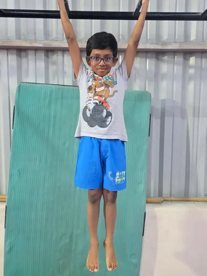 This young student builds his strength by hanging from the bar. This simple exercise is key for developing the muscles needed for more advanced skills on bars and rings.