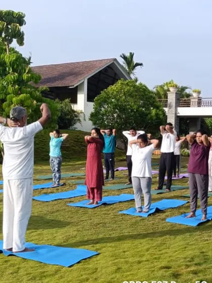 A group practices standing warm-ups on the lawn. These simple movements prepare the joints and muscles for the yoga session ahead.