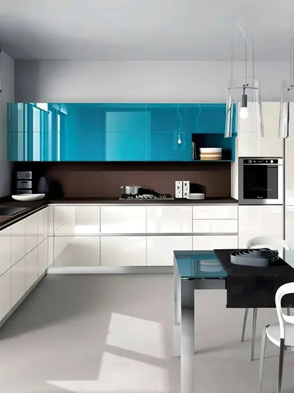 A contemporary kitchen design that pairs glossy white cabinets with a striking blue accent panel. The open layout includes a dining table within the kitchen space, perfect for modern, informal living.