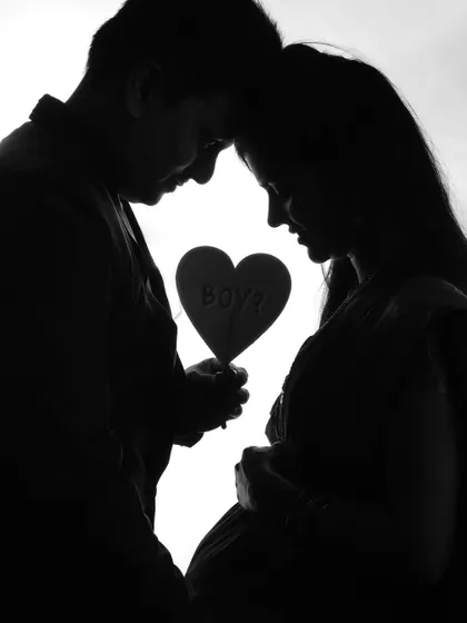 A beautiful silhouette of an expecting couple holding a heart-shaped sign. This artistic black and white shot is a creative way to announce they are expecting a baby boy.