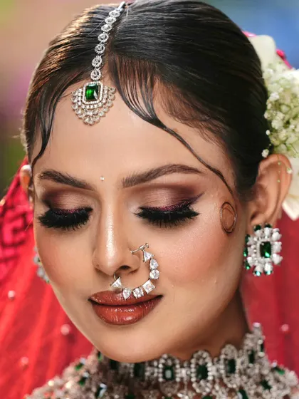 A close-up of a stunning bridal look, featuring a nude smokey eye with a defined brown crease. This style perfectly complements a traditional red lehenga and emerald jewelry, creating a modern yet classic feel.