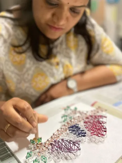 Another angle showing the careful and focused work that goes into creating a detailed string art piece.