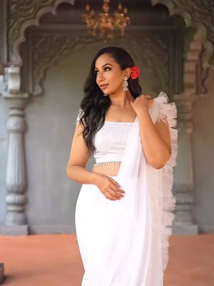 A modern take on a classic look. For this shoot, I paired a glamorous makeup style with a contemporary white ruffled saree, adding a red rose for a pop of color.