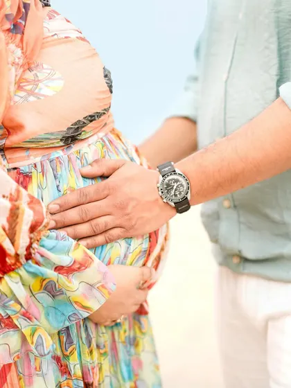 A close-up detail shot of the partner's hand gently resting on the baby bump during a beach session.