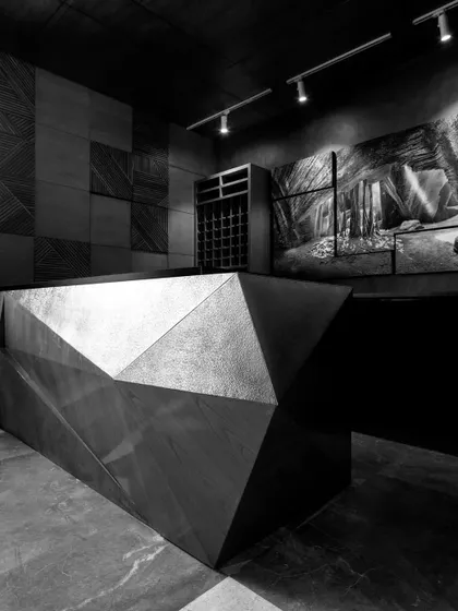 A monochrome shot of the modern cubism bar at The Restaurant at Hibiscus, designed and executed by Furgonomics. The faceted brass form stands as a beacon of sophistication against the textured backdrop.