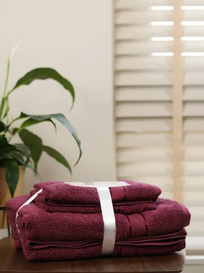 A set of maroon towels in the same serene bathroom setting. We shoot product variations consistently to ensure a cohesive look for your e-commerce store.