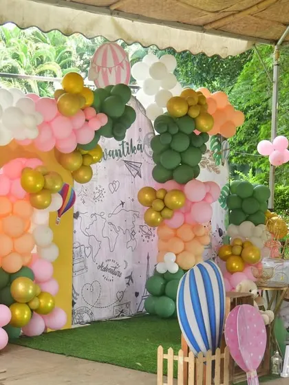 This outdoor world map themed party is perfect for a little adventurer. The setup includes a large arch with a map backdrop, colorful balloons, and fun props like a surfboard and teddy bears.