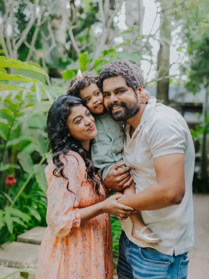 A happy family portrait taken in a garden. The daughter gives her dad a hug from his shoulders, a sweet and playful interaction.