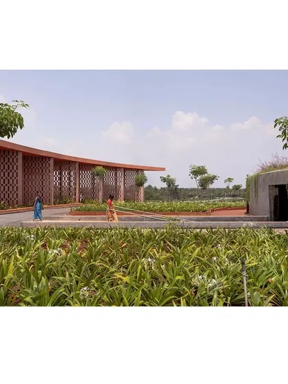 Local residents walk through the landscaped grounds of the memorial. The design uses a curved brick jali wall to create a gentle boundary, while the pathways are integrated with native plantings, making the complex feel like a natural extension of its rural surroundings.