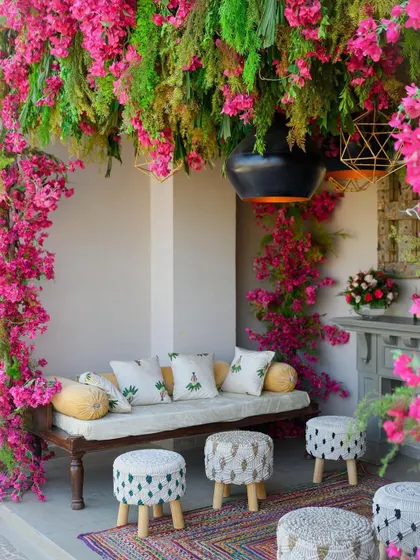 A boho-chic seating nook for a mehendi, with a ceiling of hanging greenery and bougainvillea, complemented by macrame stools.