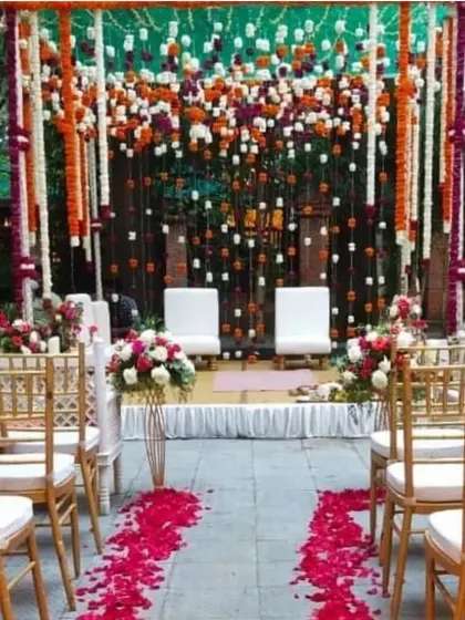 A view down the aisle towards the colorful hanging flower mandap, with rose petals lining the path for the couple's entrance.