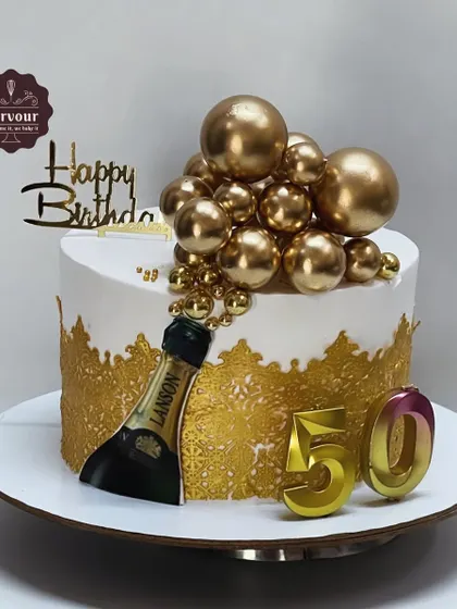 A glamorous 50th birthday cake featuring a champagne bottle, gold bubble decorations, and an intricate gold lace design. This cake is perfect for a grand and stylish celebration.