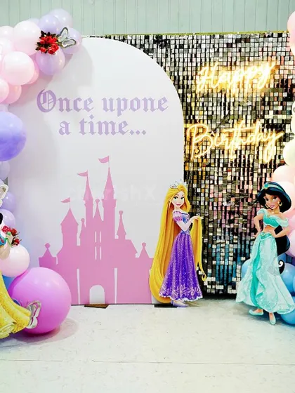 A "Once upon a time" princess party backdrop. The setup includes a silver shimmer wall and cutouts of Snow White, Rapunzel, and Jasmine.