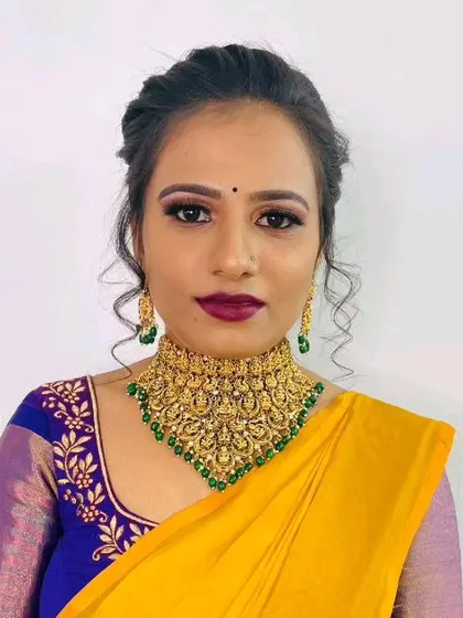A model wearing a traditional South Indian temple jewellery choker with green beads, paired with a yellow and blue silk saree.