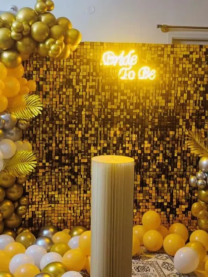 A dazzling 'Bride to be' photo booth. The backdrop is a gold sequin wall with a neon sign, framed by a balloon garland in shades of gold, yellow, and silver.