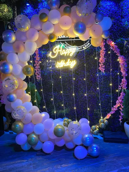 A similar elegant birthday balloon ring, shown in a darker lighting to highlight the neon sign and fairy lights.