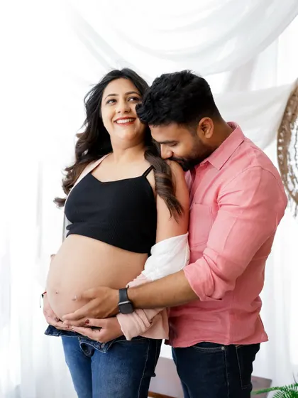 A candid and joyful moment between partners. The dad-to-be's playful kiss on his partner's shoulder brings a beautiful, natural smile to her face.