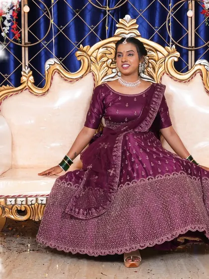 A full-length shot of the bride-to-be on the elegant white and gold sofa provided for the stage. The royal blue backdrop makes her purple lehenga pop.