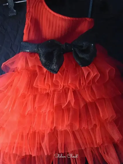 A close-up of the custom-made red ruffled frock. It features a one-shoulder design and a sequined black bow, perfect for a fun and stylish party look for kids.