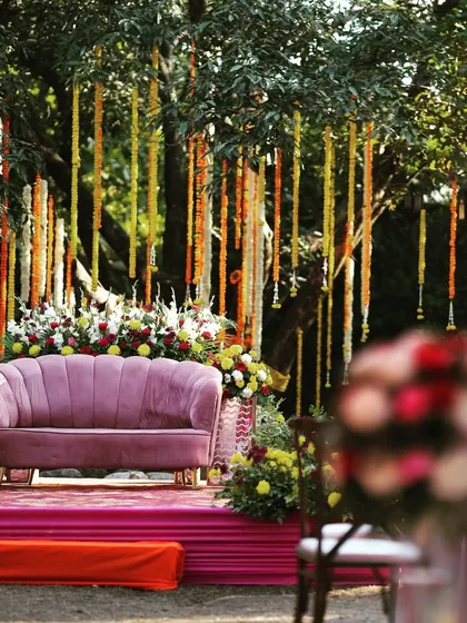 A beautiful seating area for a Mehendi function, with a mauve-pink sofa set against a backdrop of hanging floral strings.