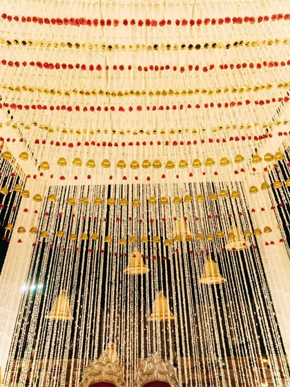 A close-up of the mandap ceiling, intricately decorated with strings of jasmine and marigolds interspersed with golden temple bells, a nod to traditional Indian temple architecture.