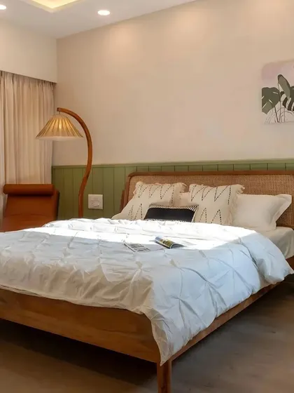 A bedroom from the Tata Aquila project, where a neutral palette is accented with a soothing green wall panel. The design uses a cane and wood bed frame to bring in natural, earthy textures.