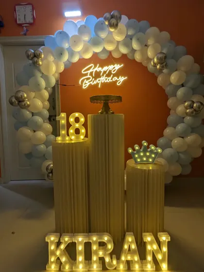 An 18th birthday party with a blue and white balloon arch, marquee number '18', and light-up letters for the name.