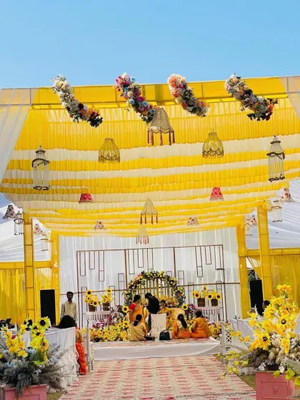 A grand tent setup for a Haldi ceremony, with yellow and white drapes creating a bright and airy feel. The view shows the entire length of the venue, leading to the main stage.