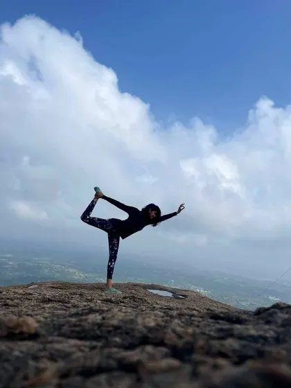 Holding the dancer's pose on a rocky summit, feeling on top of the world with the clouds below. This is the reward after a challenging and mindful trek.