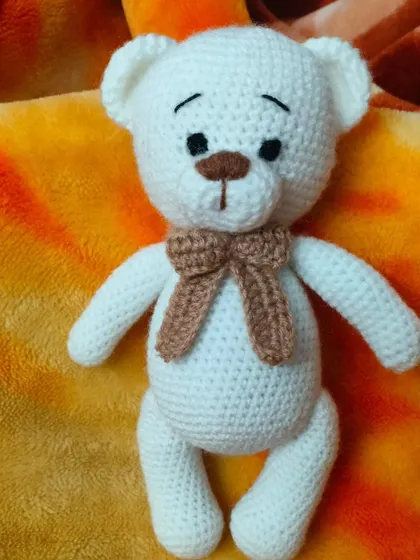 A sweet, handmade white teddy bear with a brown bow. He has a gentle expression and is perfect for comforting hugs.